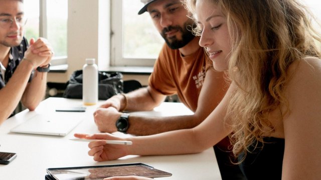 Drei Personen an einem Tisch mit Tablet in einer Besprechung
